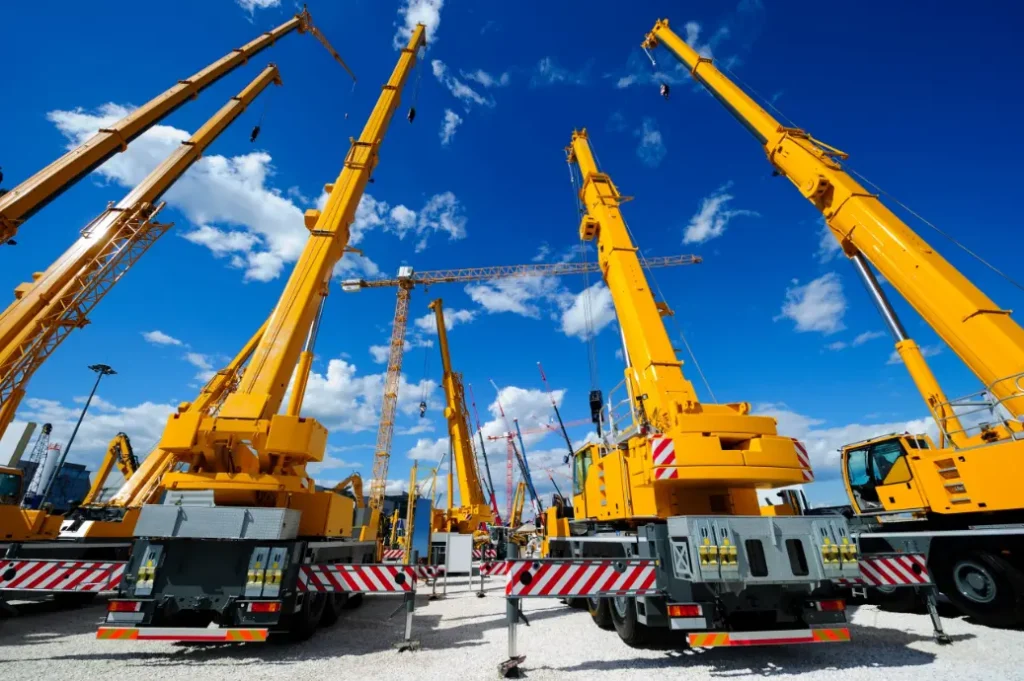 A cluster of orange crane trucks parked at a construction site, awaiting use.
