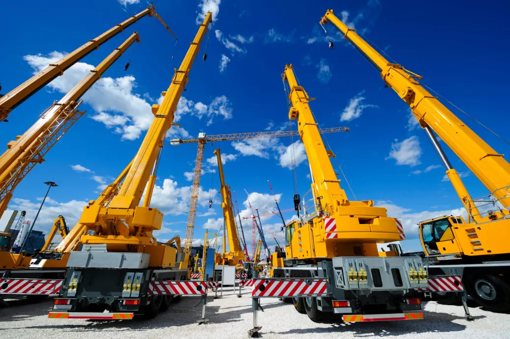 A cluster of orange crane trucks parked at a construction site, awaiting use.