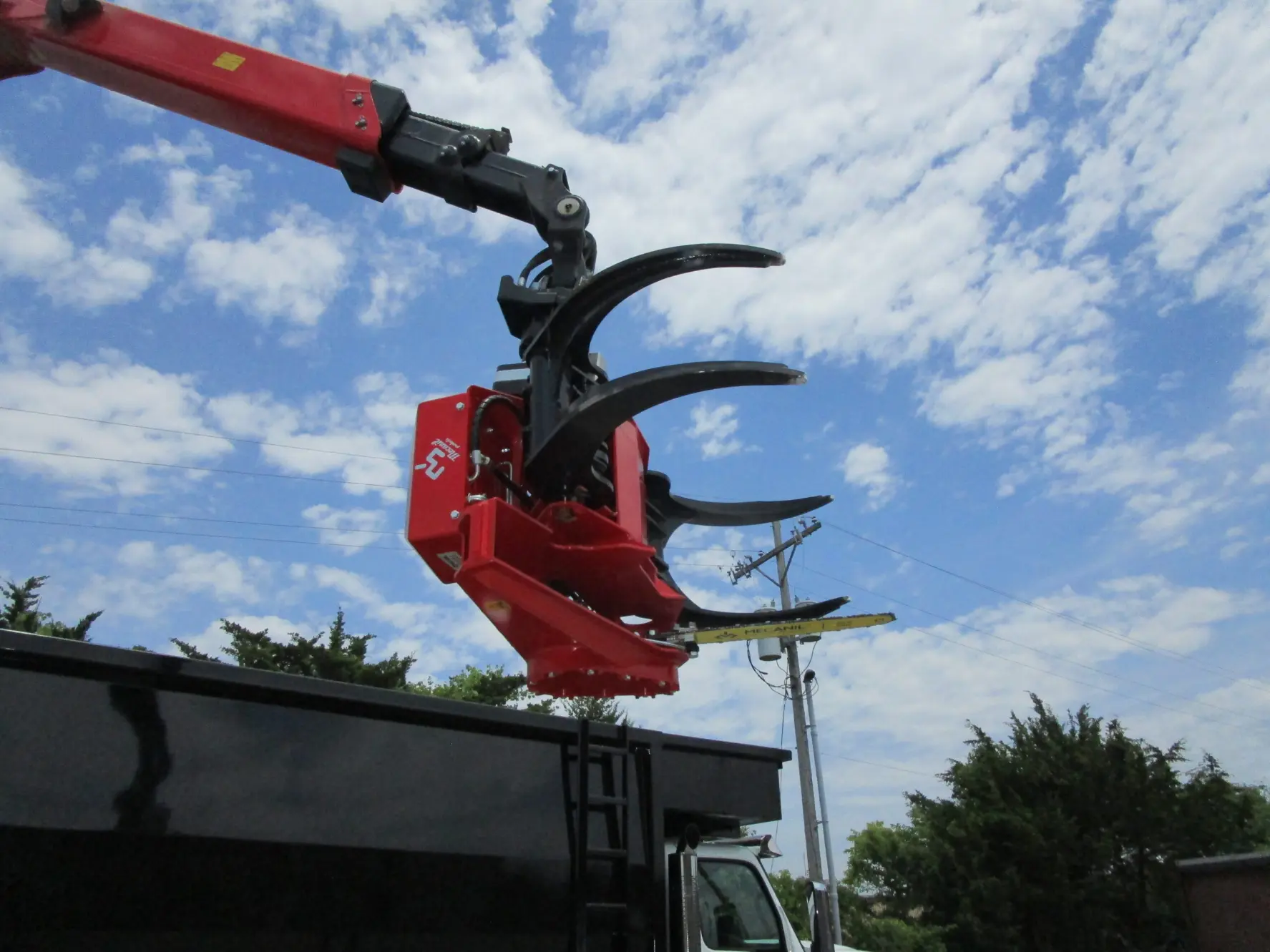 A large red tree cutting crane mounted on a truck, ready for operation in a wooded area.
