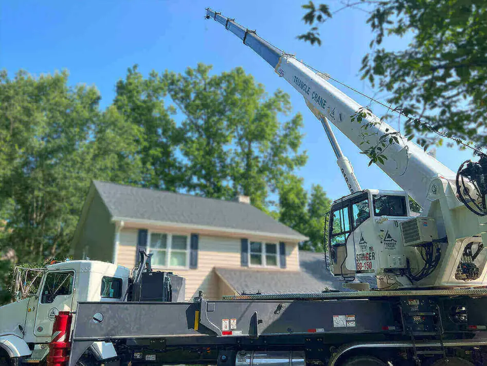 A white triangle crane positioned in front of a house, hoisting a truck onto a trailer.