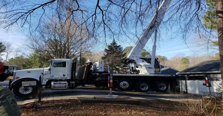 A white crane truck from Triangle Crane parked outside a house, indicating preparation for lifting or construction tasks.
